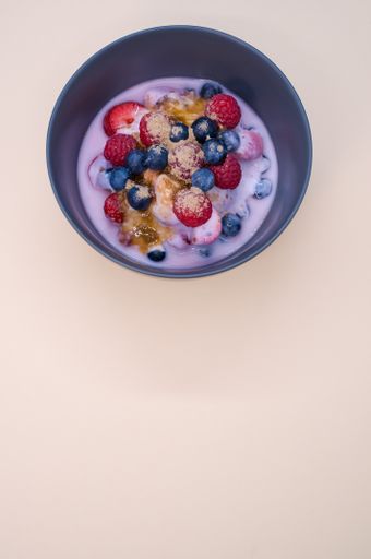 A bowl of yogurt with raspberries, blueberries, and powder isolated on a cream background