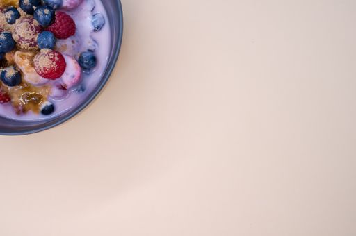 A top view of yogurt with raspberries, blueberries, and powder on bowl isolated on cream background