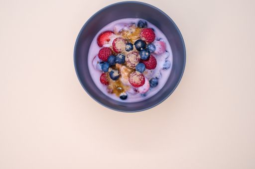 A top view of yogurt with raspberries, blueberries, and powder on bowl isolated on cream background