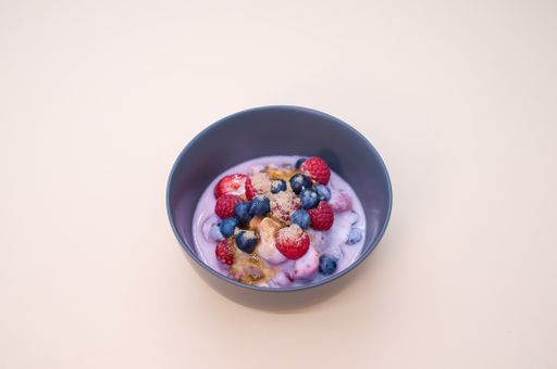 A top view of yogurt with raspberries, blueberries, and powder on bowl isolated on cream background