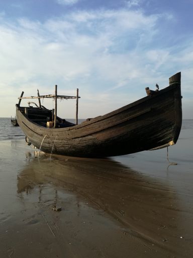 A vertical shot of an empty wooden boat on a sandy shore