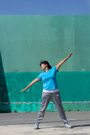 A Latina woman stretching with arms outspread; exercising outdoors