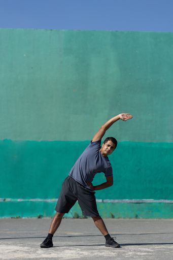 A Mexican young man exercising outdoors and doing side bends