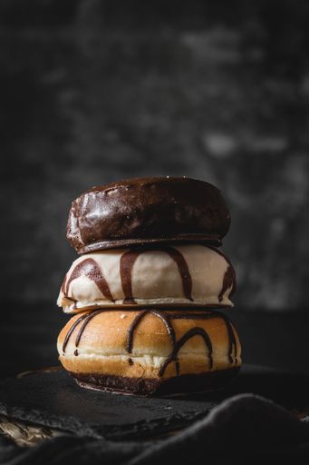 A stack of three different fresh donuts with chocolate and caramel frosting on a wooden board