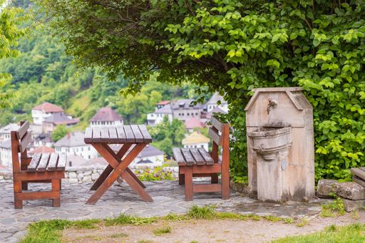 A pair of wooden benches with a table between them next to a lush tree outside on a sunny day