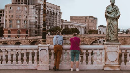 Two individuals standing on a bridge adjacent to a saintly statue of Saint Anthony