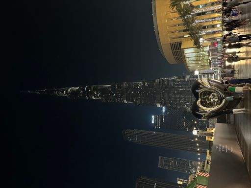 Nighttime scene of pedestrians strolling and relaxing on a vibrant Dubai sidewalk near a towering structure