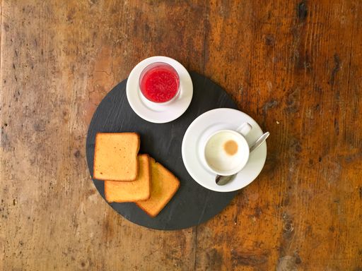 A top view shot of a strawberry jam, toasts, and a cup of cappuccino on a wooden table