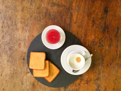 A top view shot of a strawberry jam, toasts, and a cup of cappuccino on a wooden table