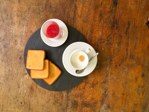 A top view shot of a strawberry jam, toasts, and a cup of cappuccino on a wooden table