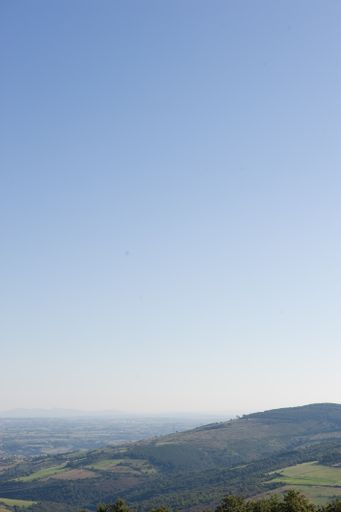 A vertical shot of a hill covered by vegetation under clear blue sky
