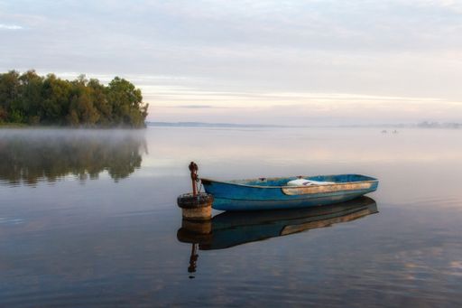 Foggy dawn over the lake. Lonely boats on the shore.
