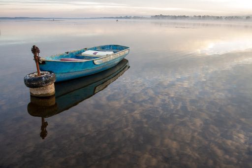 Dawn over the lake. Lonely boats on the water. Reflection of clouds in the water.