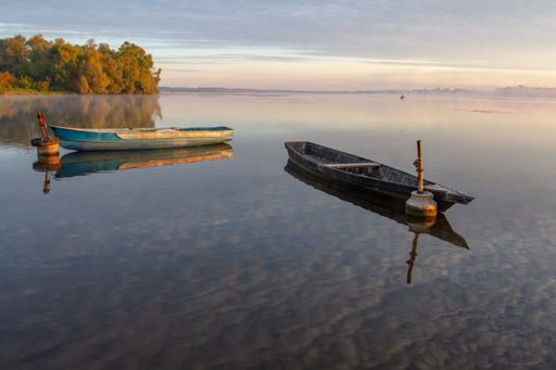 Dawn over the lake. Lonely boats on the water. Reflection of clouds in the water.