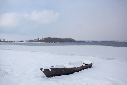 A boat covered with snow on the snowy shore of the lake