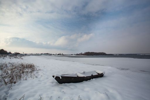 A boat covered with snow on the snowy shore of the lake