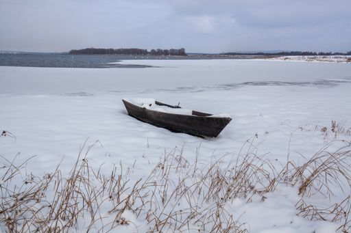 A boat covered with snow on the snowy shore of the lake.