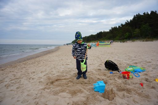 Young small boy playing with plastic toys on sand close by the water at a beach on a cloudy and windy day.