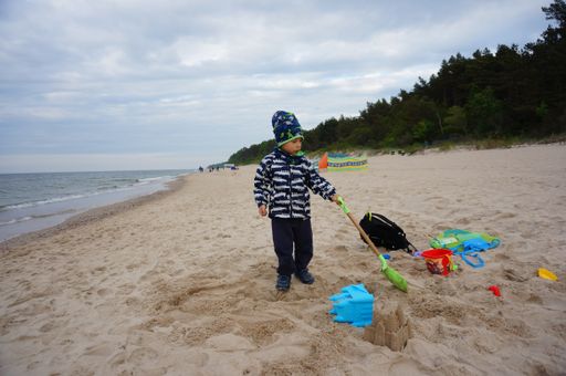 Young small boy playing with plastic toys on sand close by the water at a beach on a cloudy and windy day.