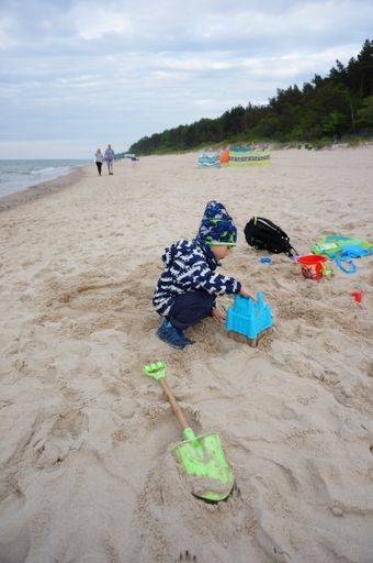Young small boy playing with plastic toys on sand close by the water at a beach on a cloudy and windy day.