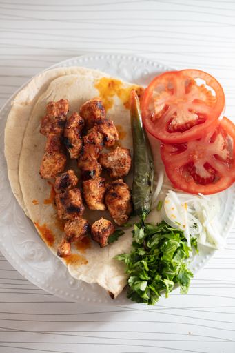A top view shot of grilled meat on a pita bread with tomato slices, green pepper and cilantro leaves