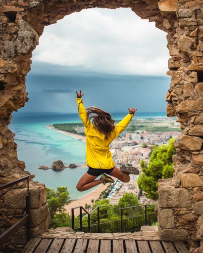 Girl with a yellow coat jumping with excitement and joyment on a doorway with the Mediterranean sea in the background