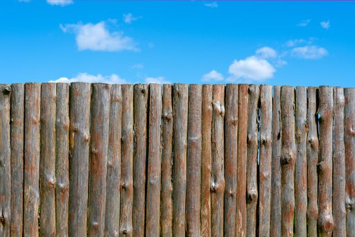 An aged wooden log fence under a bright blue sky