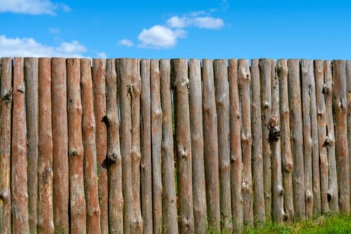 An aged wooden fence with logs under a bright blue sky