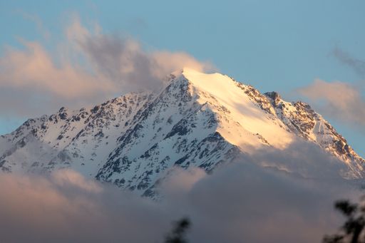 An aerial shot of mountain peaks in snow seen through clouds on a sunny day