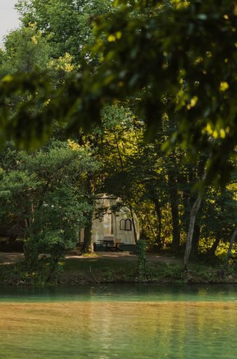 A vertical shot of a tent in a forest next to a lake surrounded by wild nature