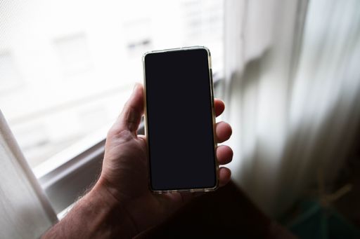A closeup shot of a hand holding a smartphone with a blank screen on a blurred background