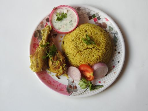 A closeup shot of delicious homemade Chicken Biryani with rice and a bowl of yogurt dip