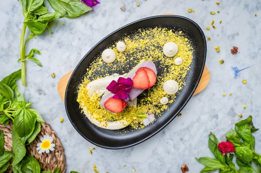 A plate with Vegan blueberry matcha cake topped with strawberry on the side pistachios. Served on a plate with fruits around.