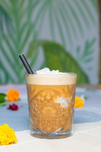 A cup of iced coffee latte with flowers in the backdrop on a table.