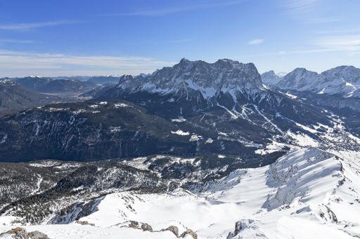 View from top of a mountain to Zugspitze (highest mountain of Germany) at a beautiful day in winter. Wild snowy alpine landscape with blue sky. Tirol,