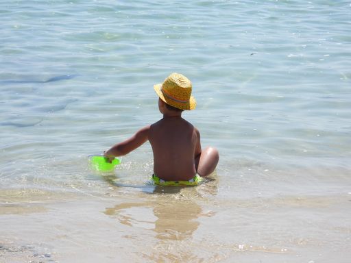 Young boy in yellow hat playing with frisbees on sandy beach