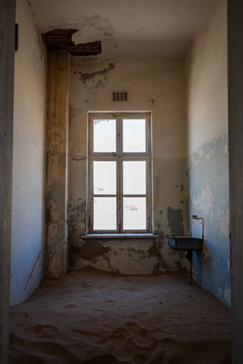 An aged, dilapidated room with a big window in an old desert town