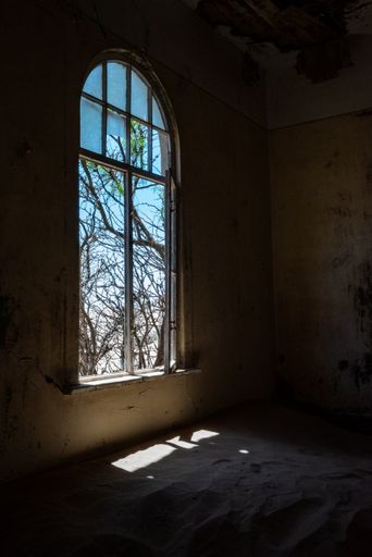 An aged, dilapidated room with a big window in an old desert town