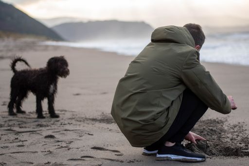 A young man with his Irish Water Spaniel making a sand castle on the beach at daylight