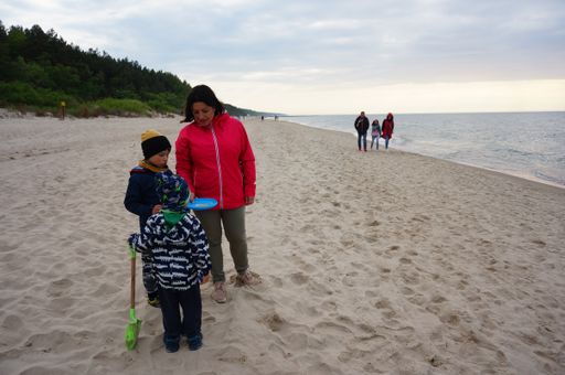 Woman and two kids standing on sand at a beach in the afternoon.