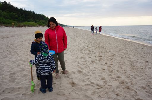 Woman and two kids standing on sand at a beach in the afternoon.