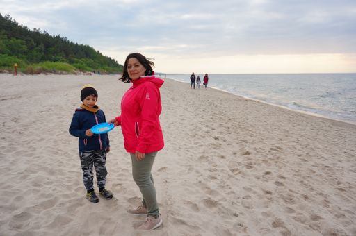 Woman and two kids standing on sand at a beach in the afternoon.