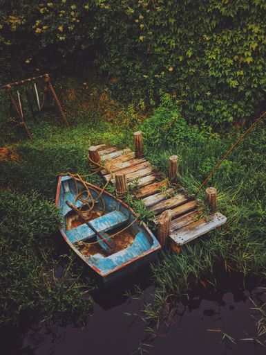 A vertical shot of an old boat in the water near a wooden dock surrounded by greenery
