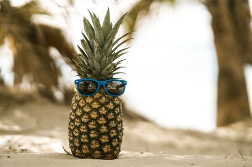A funny photo of a pineapple with sunglasses under palm trees at a sandy beach