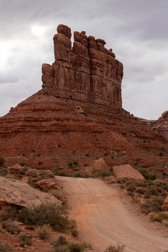 A vertical shot of a dirt road in the desert leading to a rock formation in Monument Valley, Utah