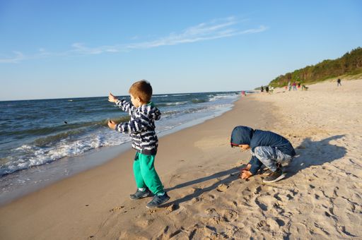 Two Polish young boys playing with sand close by the water at a beach on a cloudy and windy day.
