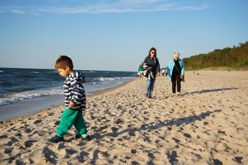 Young small Polish child playing on sand close by the water at a beach on a windy and cloudy day.