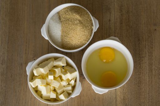 A top view of different ingredients of a cookie in white bowls put on a wooden kitchen table