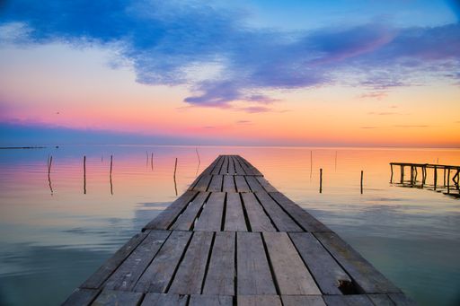 A scenic view of a wooden pier over a lake at sunset