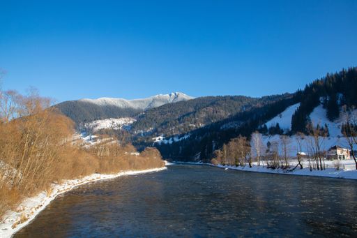 River flowing through snowy landscape with trees and mountains in the backdrop